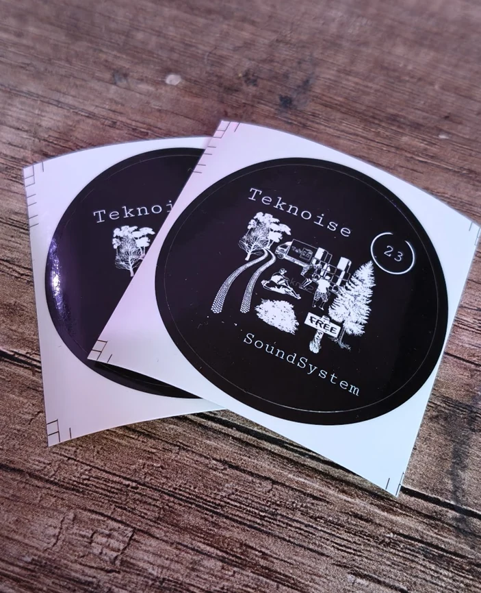 Twee zwarte ronde stickers met wit ontwerp op een houten ondergrond