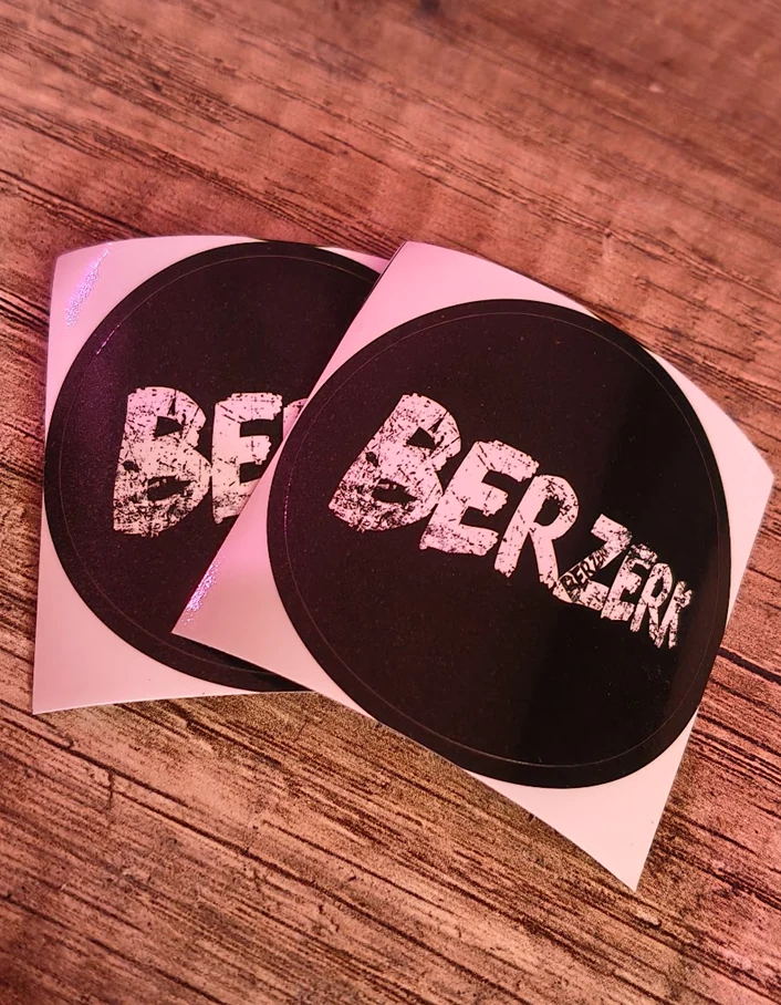 Twee zwarte ronde stickers met witte BERLIJN-opdruk op een houten ondergrond